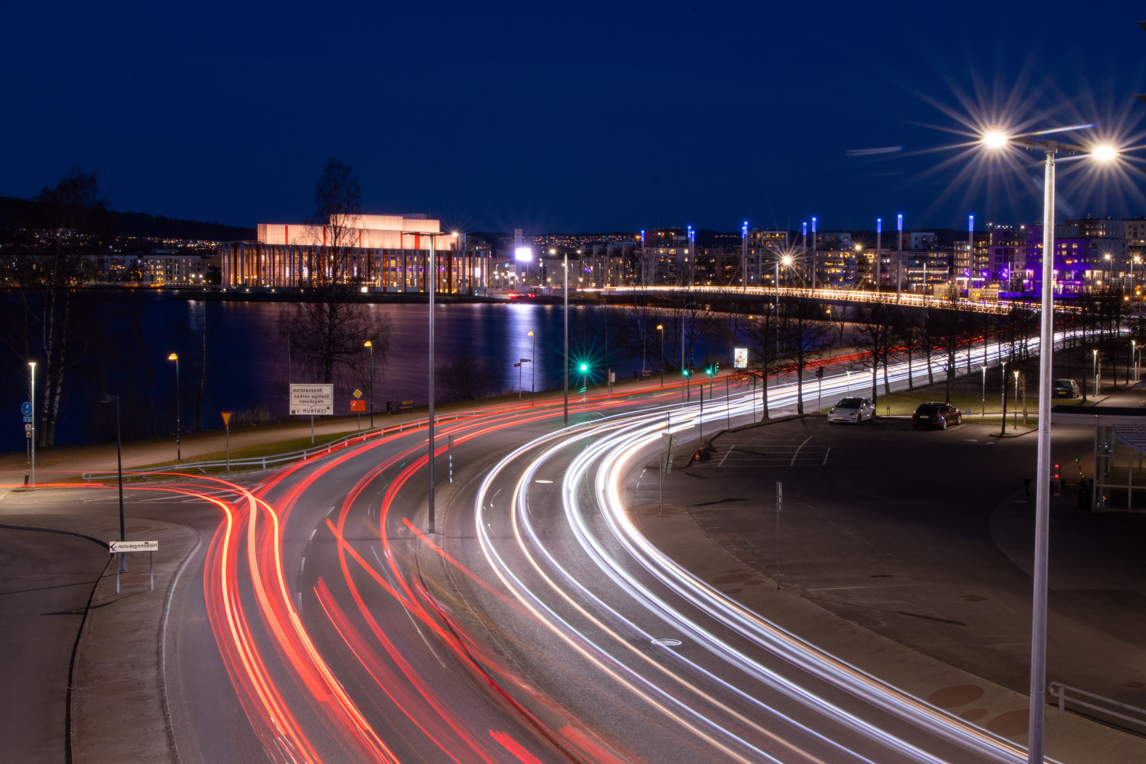 Stad i skymning med ljusspår från trafik längs vattnet.